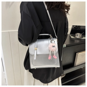 Sac bandoulière carré argenté avec porte-clés en peluche rose dans un cadre de vie