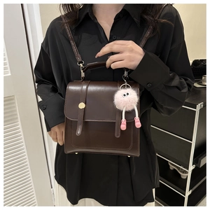 Détail d'un sac carré marron foncé avec boucles métalliques et breloque en peluche rose