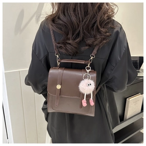 Détail du sac à dos en cuir marron foncé avec un pendentif monstre en peluche rose sur le côté