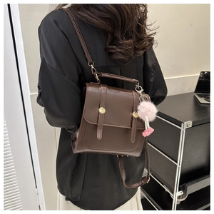 Détail du sac à dos en similicuir marron foncé avec boucles dorées et pompon rose