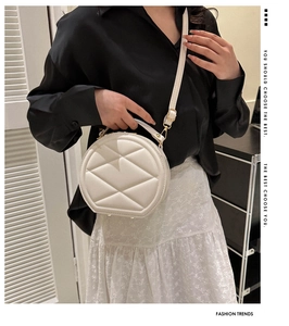 Detail of white round crossbody bag featuring quilted rhombic texture and metal buckle