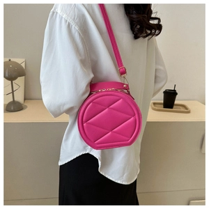 Model wearing a pink quilted round crossbody bag with leather texture and top handle