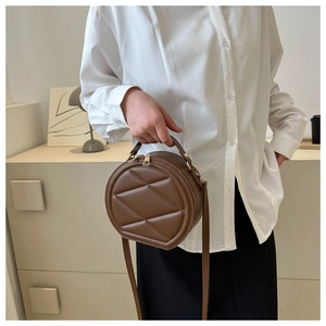 Close-up of brown round crossbody bag with quilted pattern held by a model
