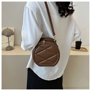 Close-up of brown quilted circular crossbody bag with gold hardware and top handle details