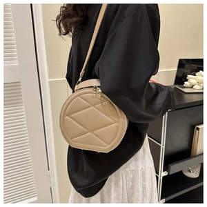 Quilted round crossbody bag in beige leather shown on model in minimalist interior setting