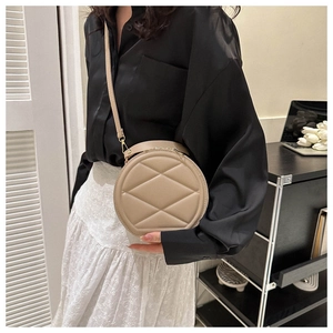 Detail view of beige quilted circular crossbody bag with gold hardware and strap