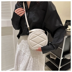 Detail view of a white quilted round crossbody bag with gold hardware and leather strap