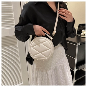 Detail of round beige crossbody bag with quilted lattice pattern and top handle design