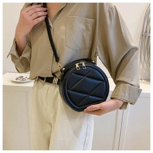 Detail of a black quilted leather round bag with gold dual zippers on a model side view