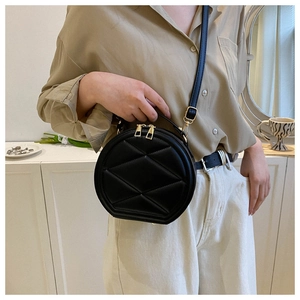 Detail view of black quilted circular crossbody bag with metal zippers and slim strap