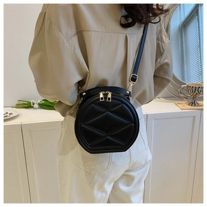 Detail of round quilted black crossbody bag with gold zippers shown on a model