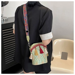 Detail of straw woven bucket bag with colorful ethnic tassels and geometric wide strap