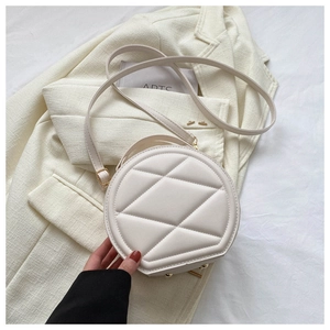 Detail of round beige quilted PU leather crossbody bag with gold zipper and metal studs