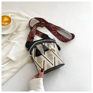 Detail of woven bucket bag with tassels and colorful embroidered ethnic strap on white cloth