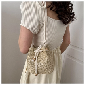 Detailed close-up of woven straw bucket bag with white cotton drawstring and golden beads