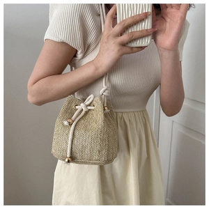 Detailed close-up of woven straw bucket bag with cotton drawstring and golden toggle charm