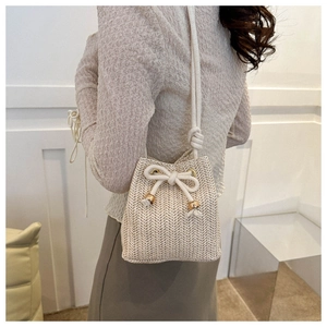 Close-up of beige woven straw bucket bag featuring drawstring closure and knot detail