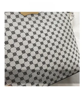 Close-up of white lychee leather with black clover pattern and gold metal hardware