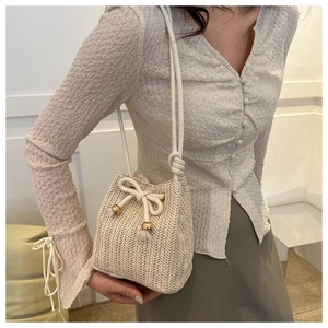 Close-up of beige woven bucket bag with drawstring closure and golden tassels