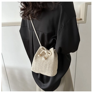 Detailed view of beige straw bucket bag featuring herringbone weave and drawstring bow