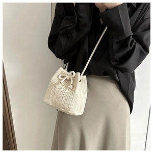 Detail of a beige woven straw bucket bag with drawstring closure and bow decoration