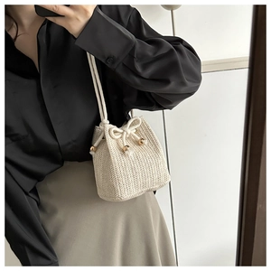 Detail of off-white woven straw bucket bag with drawstring closure and gold beads