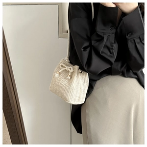 Close-up of beige woven bucket bag with drawstring closure and golden metal accents