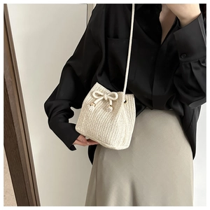 Close-up of beige woven straw bucket bag with drawstring detail and metal buckles