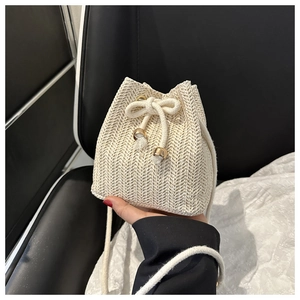 Detail of hand-woven beige straw bucket bag with white cotton drawstrings and gold hardware