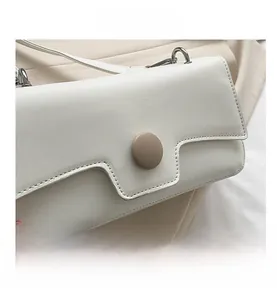 Detail of white leather shoulder bag featuring a unique tiered flap and large brown button
