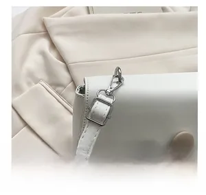 Detail of silver metal shoulder strap hooks and white leather texture on square bag