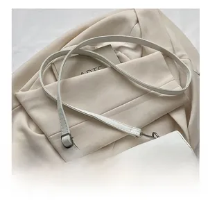 Close-up of a white faux leather crossbody bag with a round buckle on a beige blazer