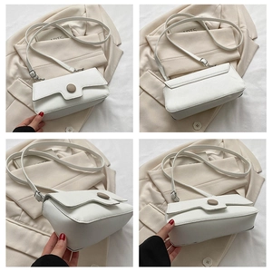 Detail view of white minimalist baguette bag with brown circular buckle and smooth leather finish