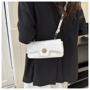 Minimalist white leather crossbody bag with a round metal clasp shown on a shoulder