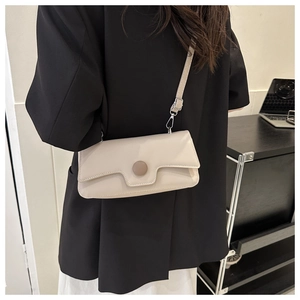 Side view of cream rectangular crossbody bag with large round button on black blazer