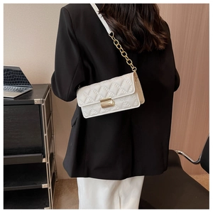 Detailed view of white quilted crossbody bag featuring gold clasp and chain strap