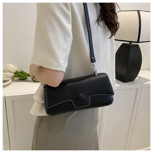 Detail of black rectangular crossbody bag with white contrast stitching and large round clasp