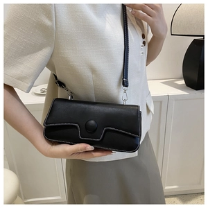 Detail of black faux leather crossbody bag with white stitching and round buckle
