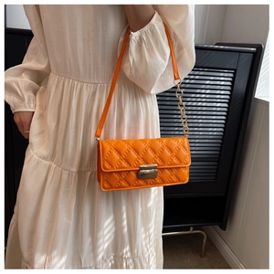 Detail of orange quilted crossbody bag with gold chain strap on a white dress model