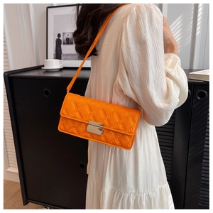 Close-up of bright orange quilted crossbody bag with metal buckle on white dress