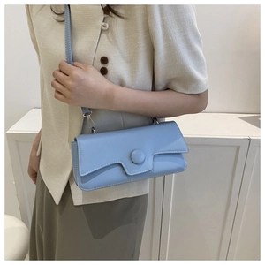 Detail of light blue crossbody bag with unique flap design and round buckle on a model