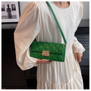 Close-up of green quilted small square bag with gold lock on white pleated dress