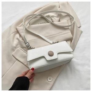Detail of white leather crossbody bag featuring a large beige button and thin strap