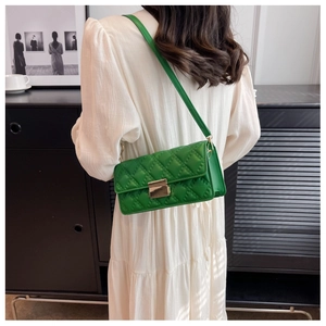 Side view of a bright green quilted crossbody bag with a gold metal lock on a white dress