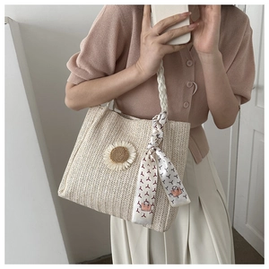 Détail d'un sac cabas en paille tissée avec applique tournesol et foulard sur la poignée