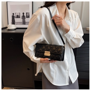 Close-up of a black quilted crossbody bag with a gold buckle worn with a white shirt