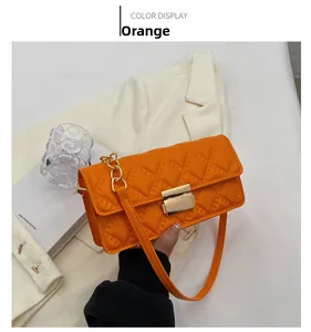 Detail of orange quilted crossbody bag with gold chain strap and metal lock closure