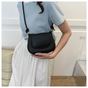 Detail of minimalist black leather saddle bag showing knot strap and metal cap on a model