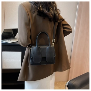 Detail van een zwarte crossbodytas met lychee-textuur gestyled met een bruine blazer en broek
