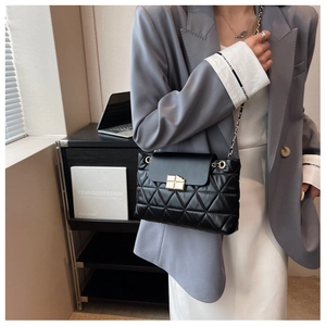 Close-up of black quilted shoulder bag with gold chain strap and metal lock closure